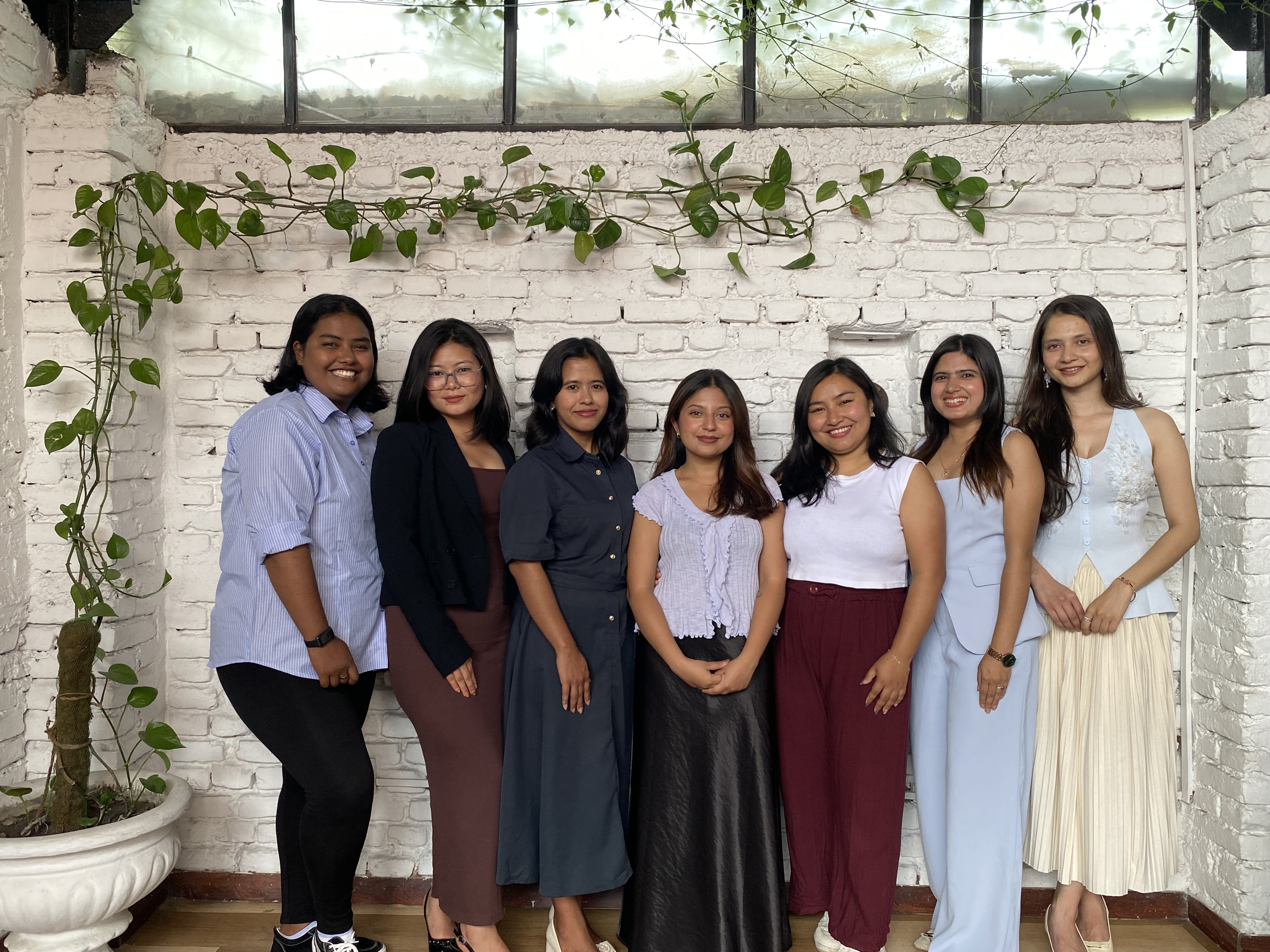 The seven co-founders of Digital Kala standing together in front of a white brick wall with hanging vines