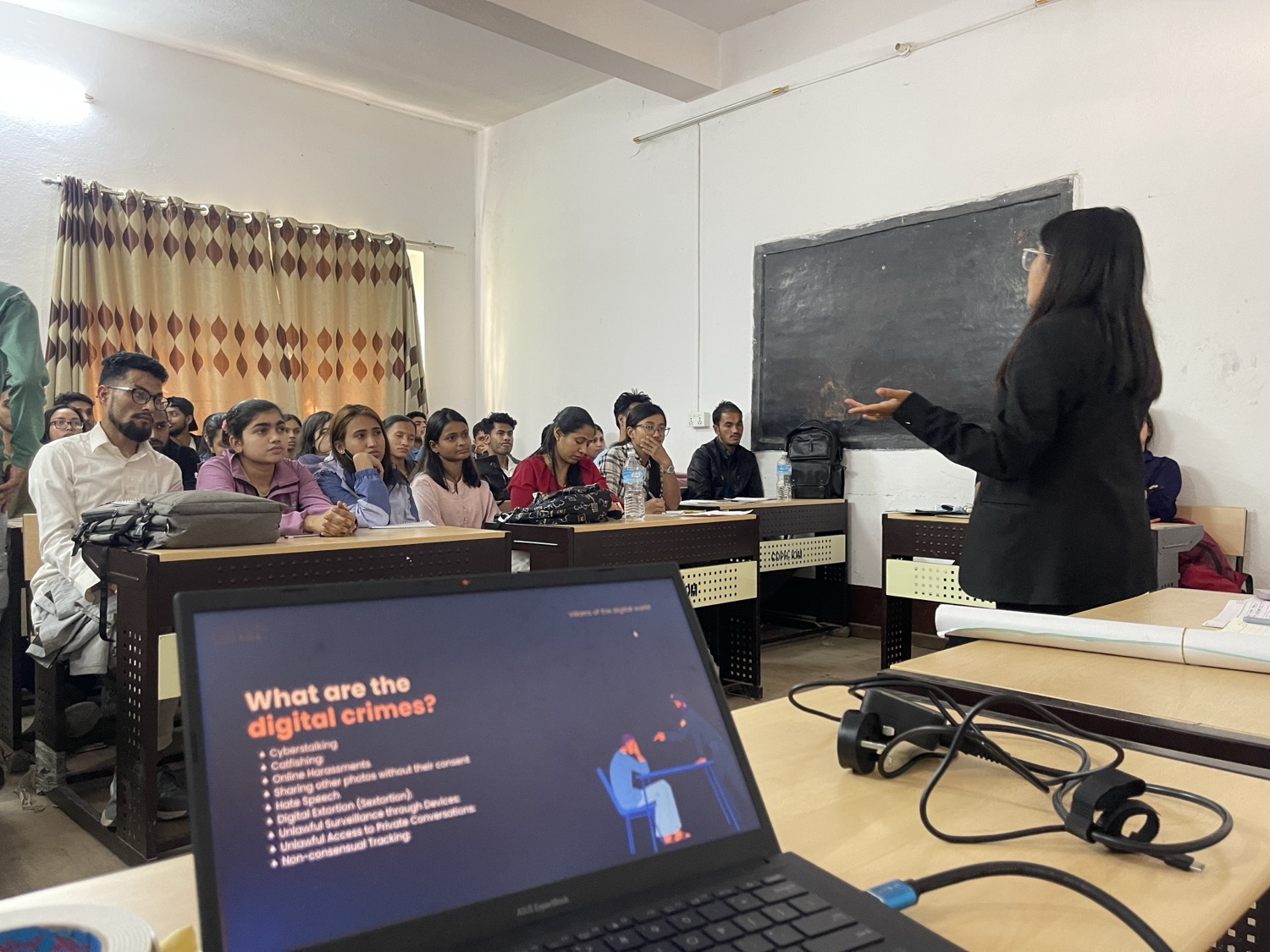 A Digital Kala facilitator leading a cyber security session at the blackboard, with a slide reading What are the digital crimes? on a laptop in the foreground and BPH students seated